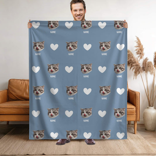 Person holding a blue blanket with cat faces and hearts pattern in a living room.