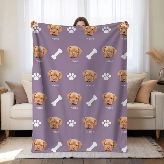 Person holding a purple blanket with a pattern of a dog's face, name, paw prints, and bones.