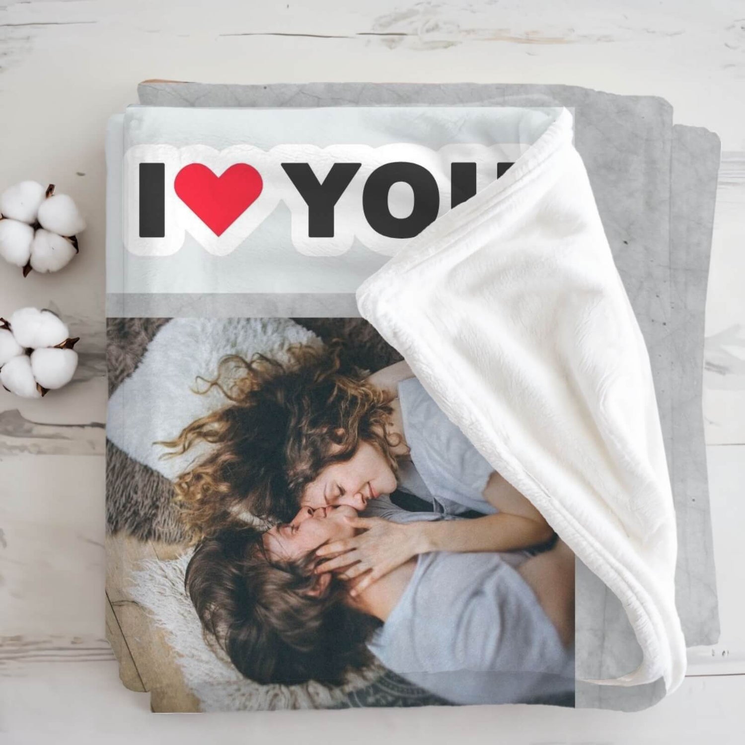 A folded light grey blanket with young couple and text "I Love You", in which the "Love" is replaced with a red heart symbol.