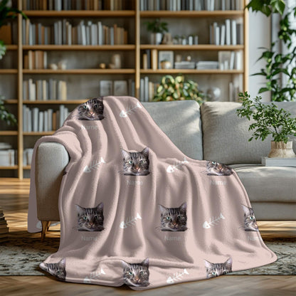 Pink blanket with cat prints draped over a gray sofa in a cozy living room.