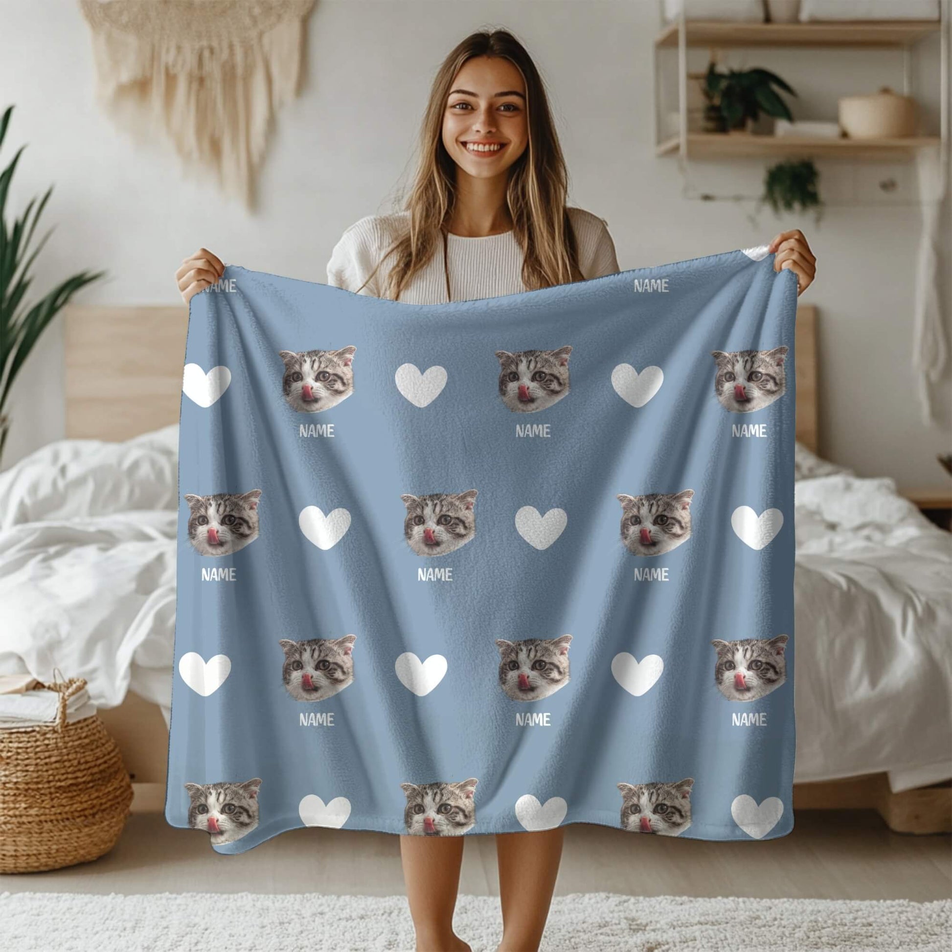 Woman holding a blue blanket with cat faces and hearts on a bed.