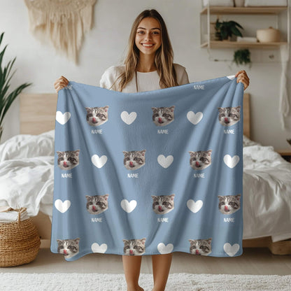 Woman holding a blue blanket with cat faces and hearts on a bed.