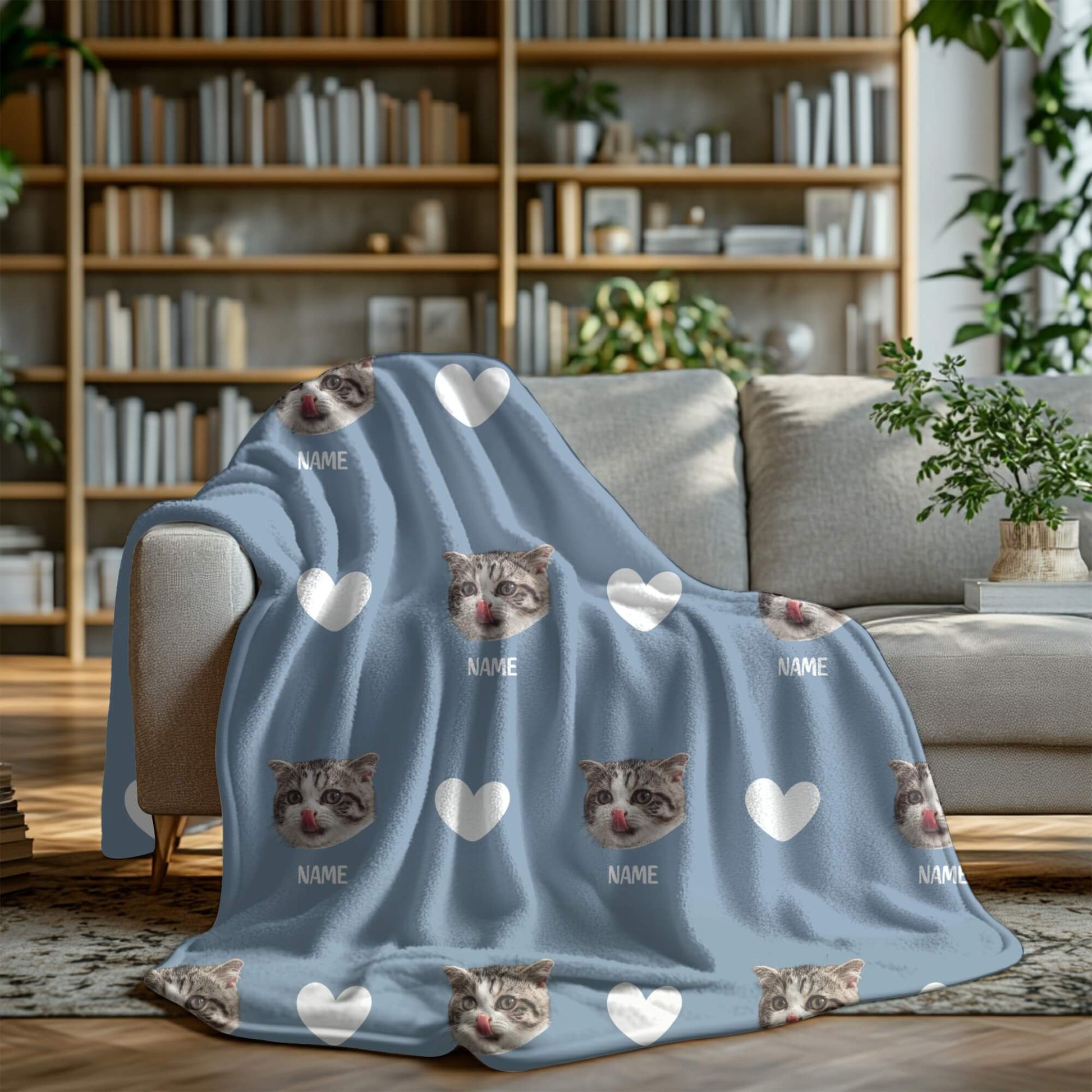 Blue blanket with cat faces and hearts on a gray couch in a living room setting.