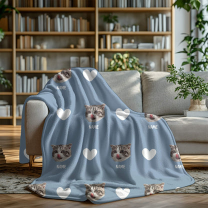 Blue blanket with cat faces and hearts on a gray couch in a living room setting.