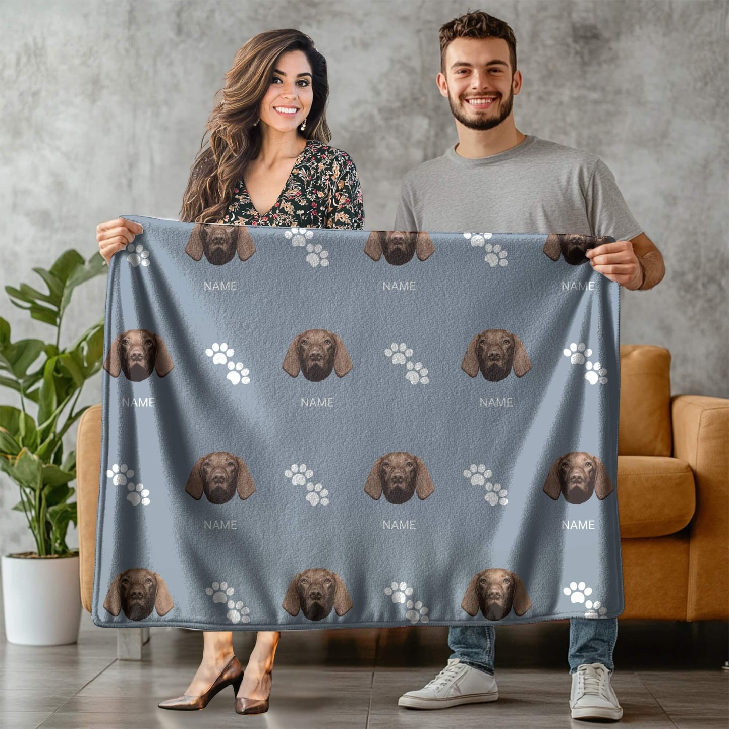 Two people holding a blanket with dog patterns and text.