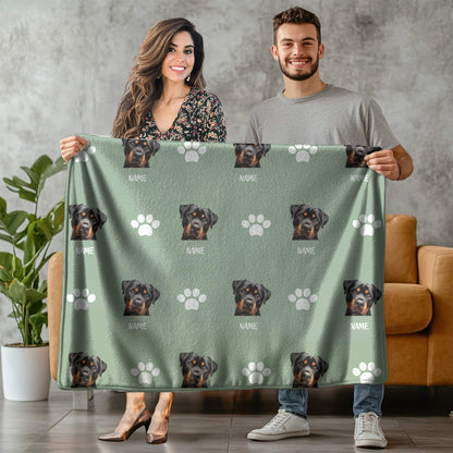 Two people holding a green blanket with dog pattern and paw prints.
