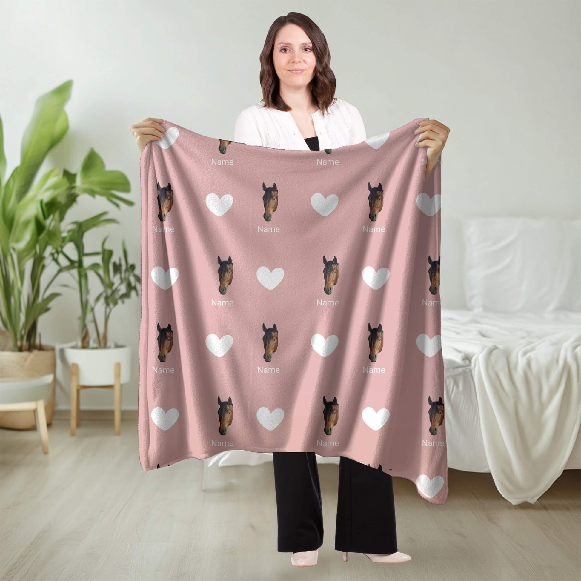 Woman holding a pink blanket with horse pattern in a room with plants and furniture.