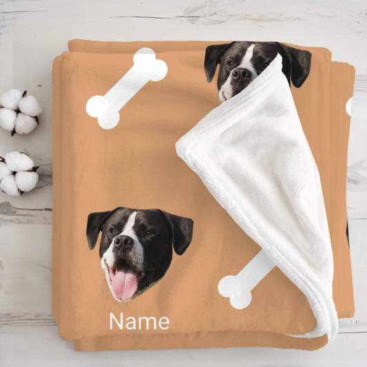 Pet blanket with a dog's face printed on it, held by another dog, on a wooden surface.