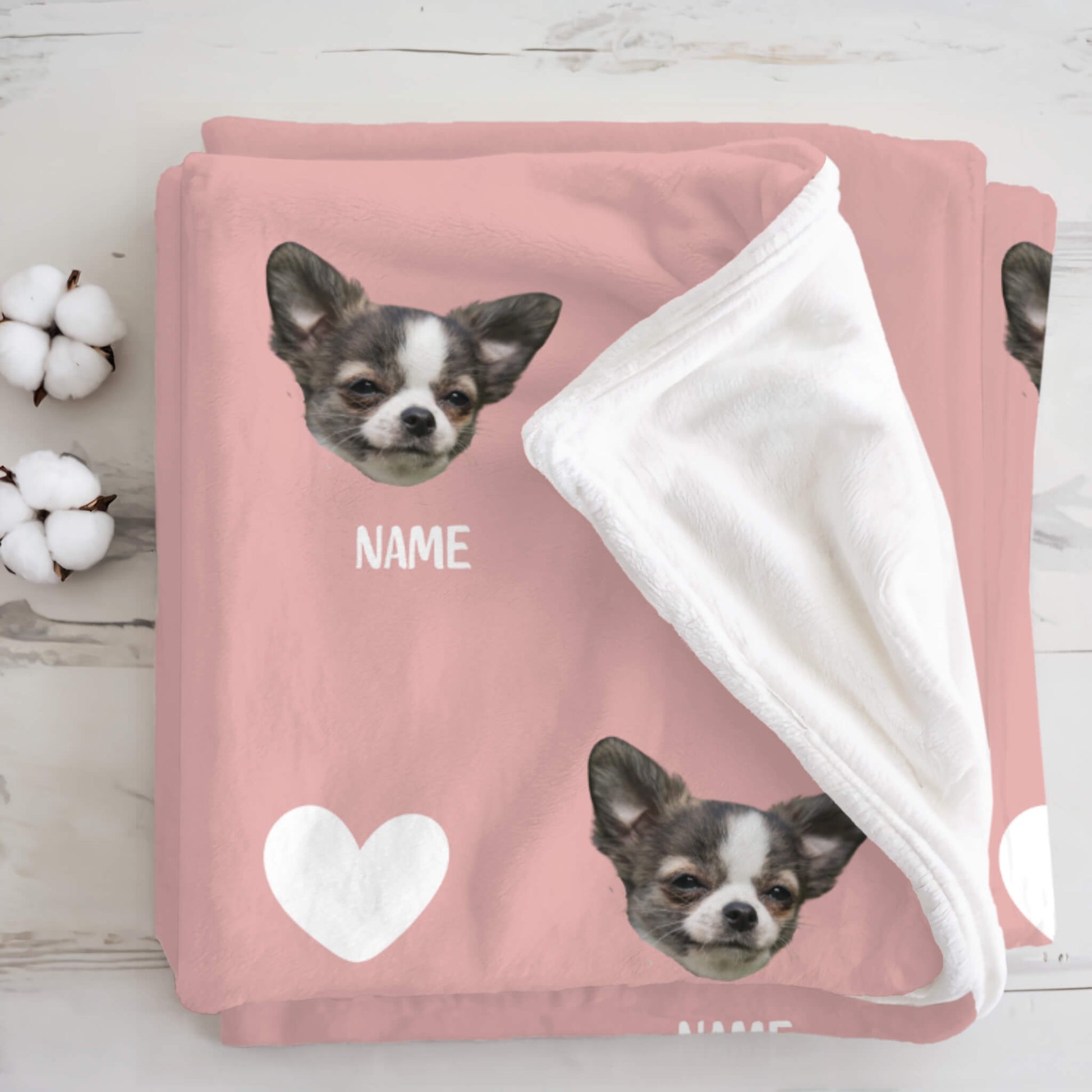 Pink blanket with a dog's face and 'NAME' text, surrounded by cotton bolls on a wooden surface.