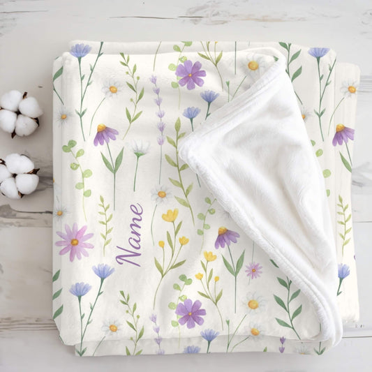 Floral-patterned blanket with a name printed on it, displayed on a wooden surface with cotton bolls.